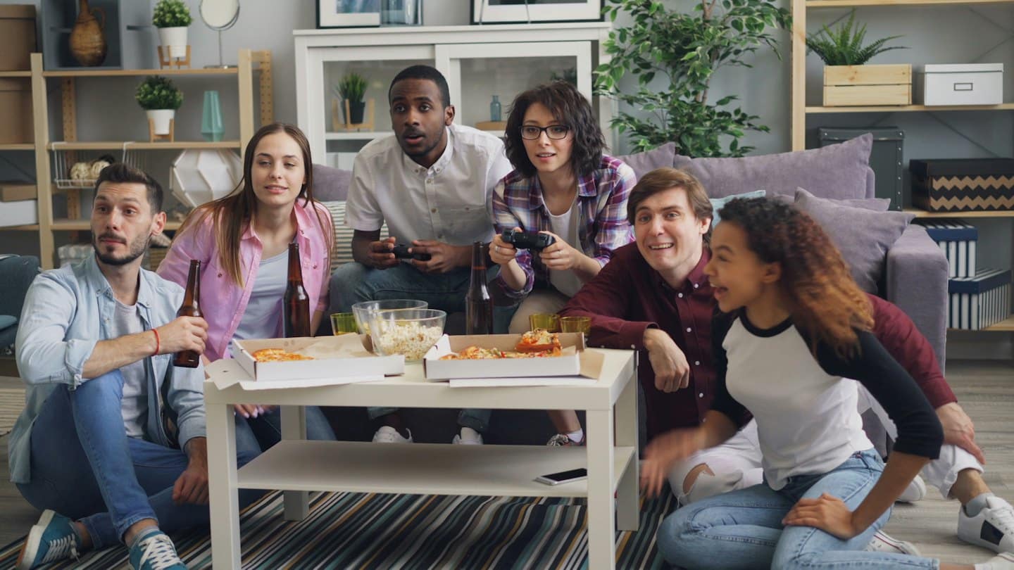 Amici giocano ai videogiochi e mangiano pizza in un soggiorno.