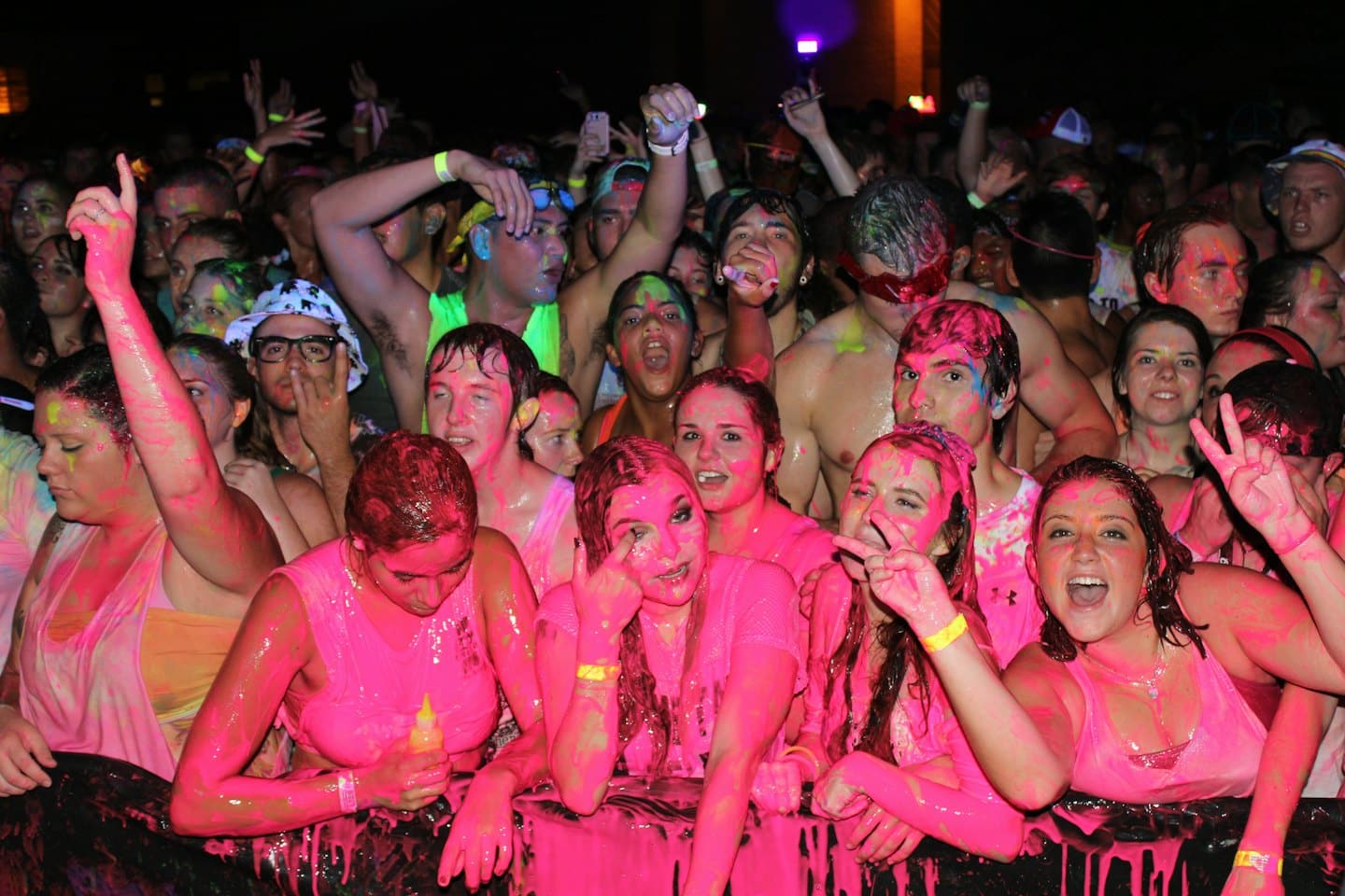 Giovani adulti coperti di vernice neon che tifano a un evento notturno.